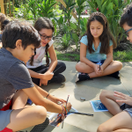 students sitting on ground in a circle while writing on large paper