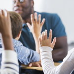 students hold up hands in class